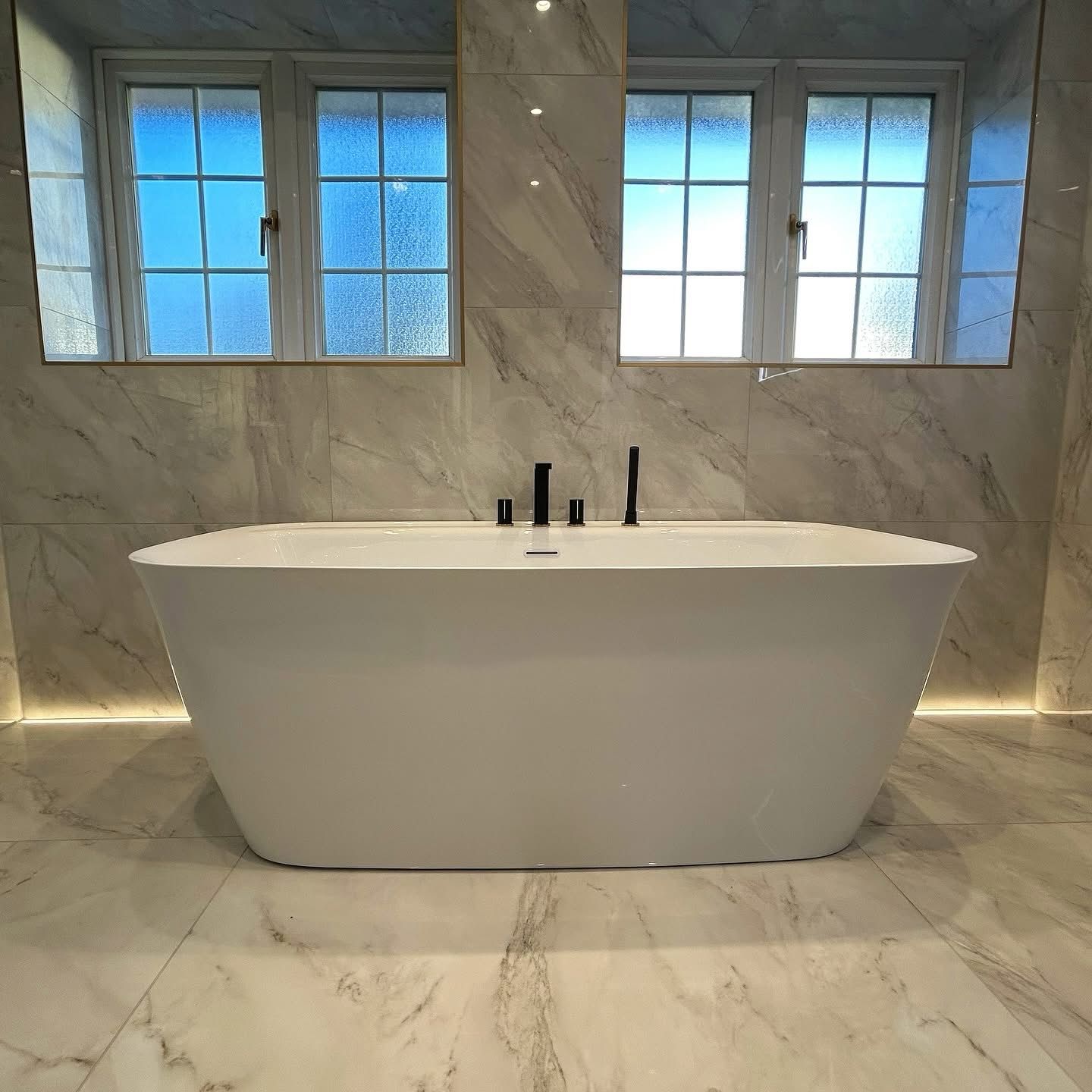 Luxury freestanding soaking tub with full marble tile walls and black hardware in Portland