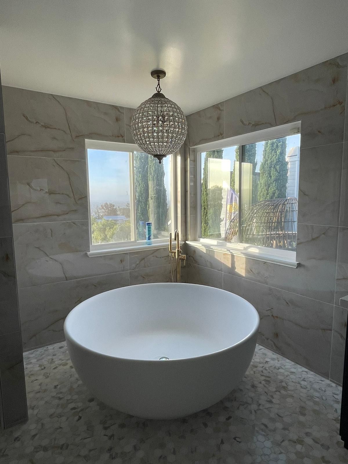 Round freestanding soaking tub under crystal chandelier with marble tile in Portland