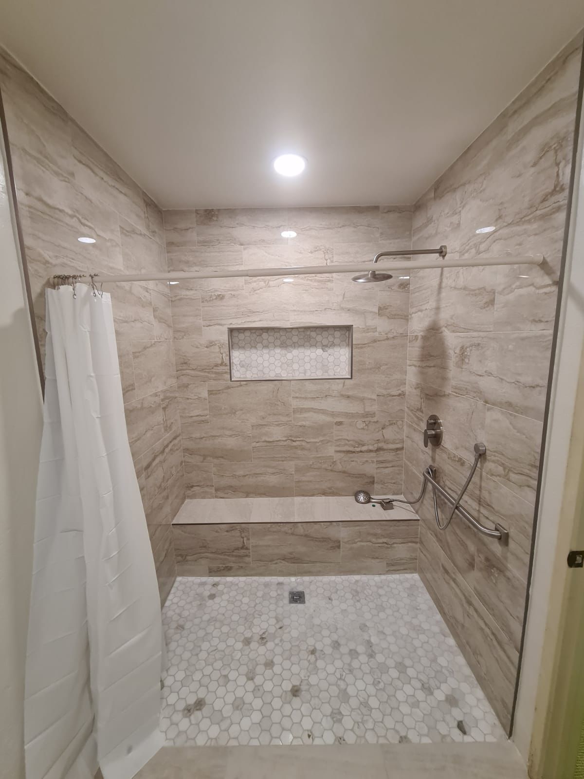 Walk-in shower with stone tile, hex floor, grab bar and tile bench in Portland